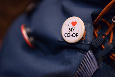 A closeup of a navy backpack with a round, white "I heart my co-op" button. 