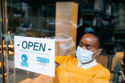 A Black small business owner places an open sign with COVID-19 restrictions in her store window.