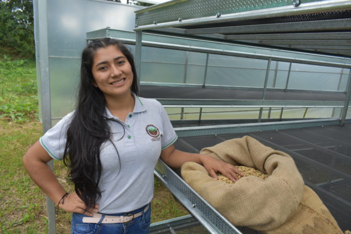 Harley wears a polo shirt with the La Prosperidad de Chirinos Coffee Cooperative logo and stands next to a burlap bag of coffee beans.